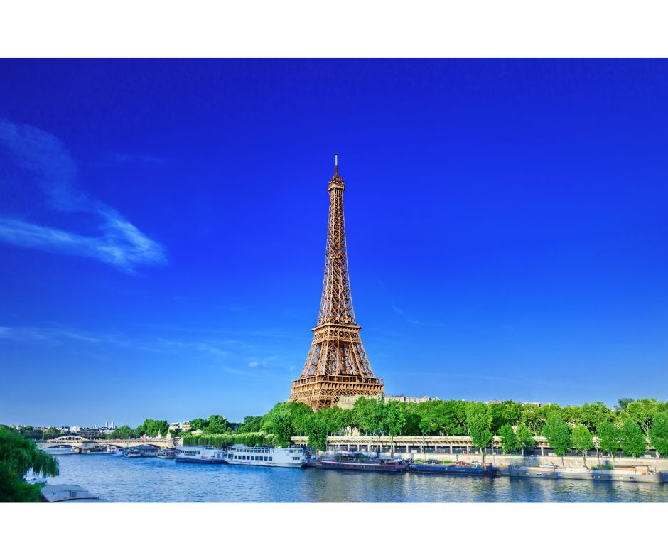 Image d'un ciel bleu avec, au premier plan, la tour Eiffel de Paris. En second plan, des bateaux-mouches sur la Seine, entourés d'arbres verdoyants.